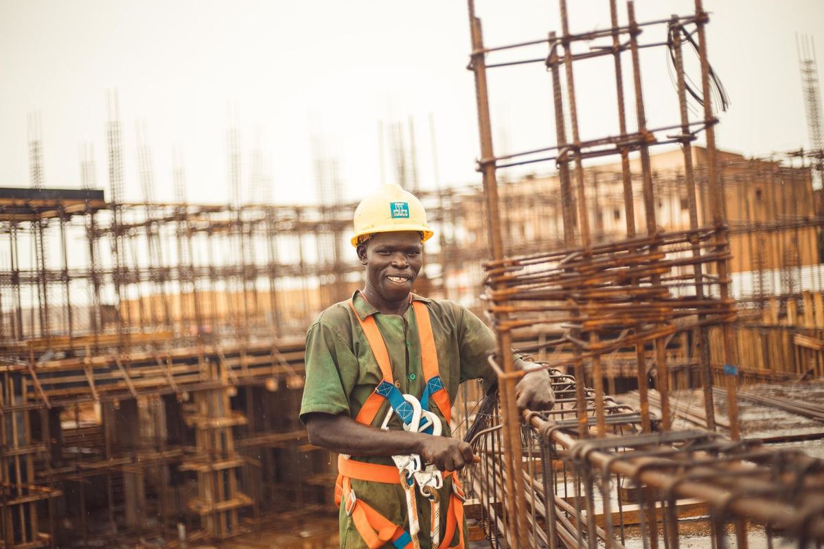 A smiling builder in a yellow hard hat at work as a new building rises around him
