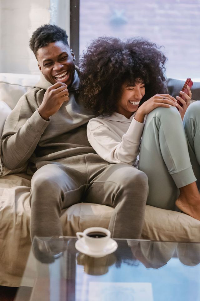 A couple laughing together over a phone on their couch