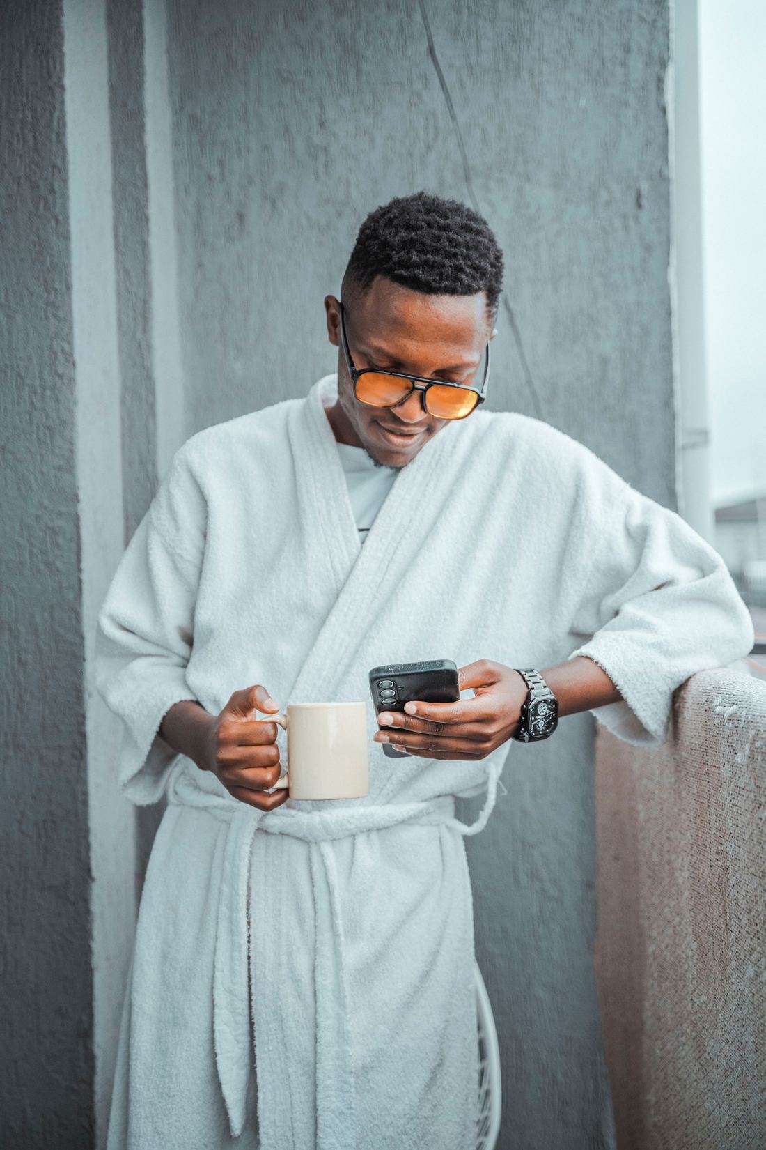 A man with coffee reading his phone on a balcony above Nairobi