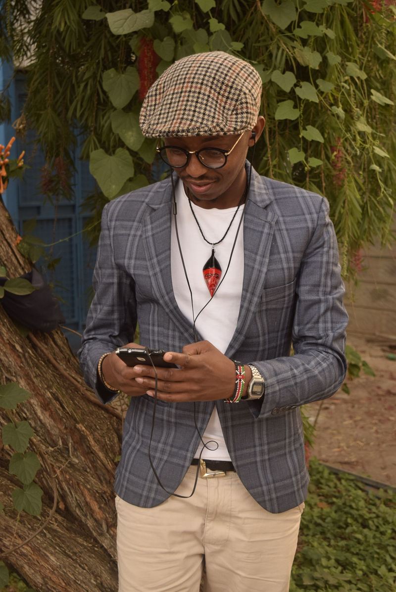 A stylish man reading his phone under the trees in Nairobi